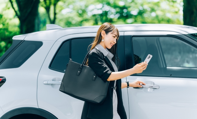 車の隣でスマホをいじる女性の画像
